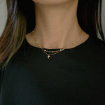 Model wearing a dainty crystal cross necklace layered with multiple pearl on gold chain necklace