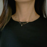 Model wearing a dainty crystal cross necklace layered with multiple pearl on gold chain necklace