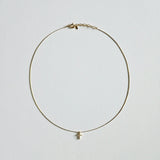 Dainty crystal cross necklace in gold laid flat on soft background with sleek snake chain