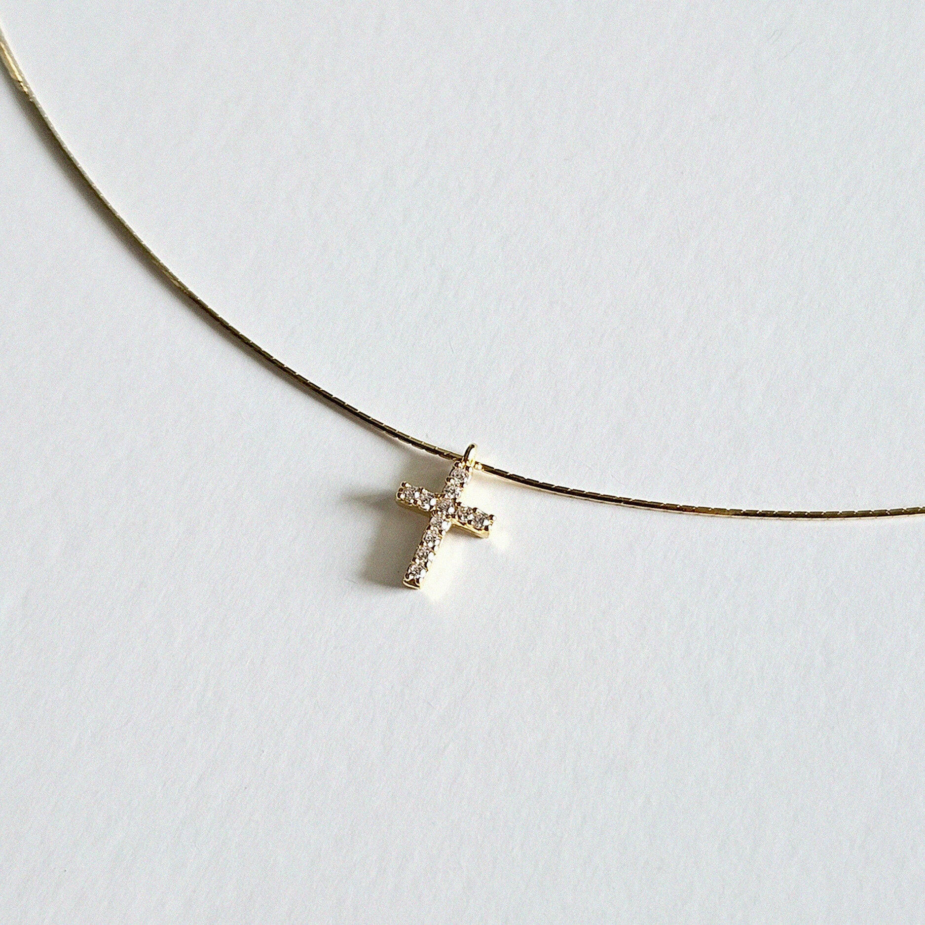 Close-up of cubic zirconia cross on fine gold snake chain with polished finish
