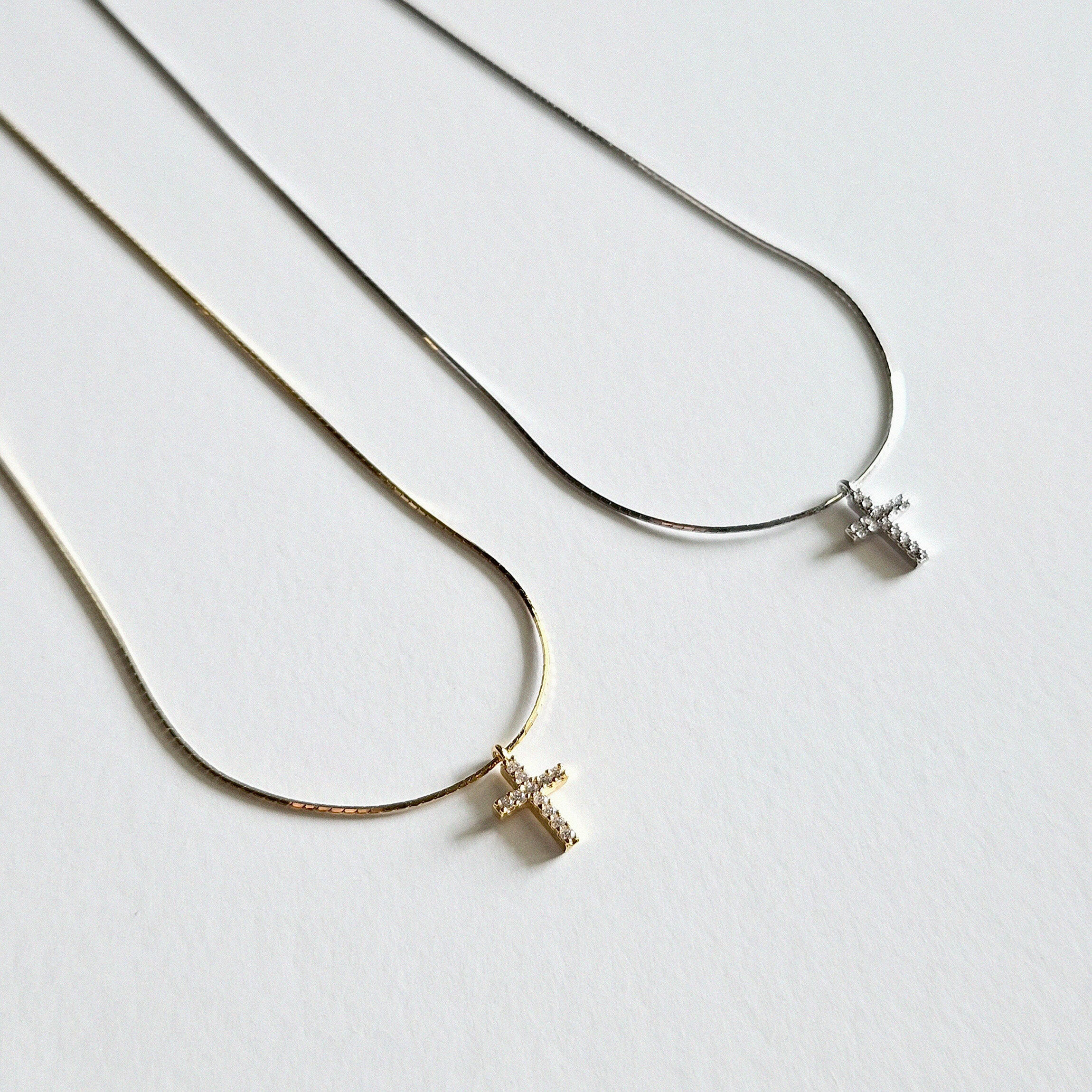 Gold and silver cross pendant necklaces displayed side by side showing sparkle detail