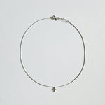 Dainty crystal cross necklace in silver laid flat on soft background with sleek snake chain