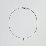 Dainty crystal cross necklace in silver laid flat on soft background with sleek snake chain