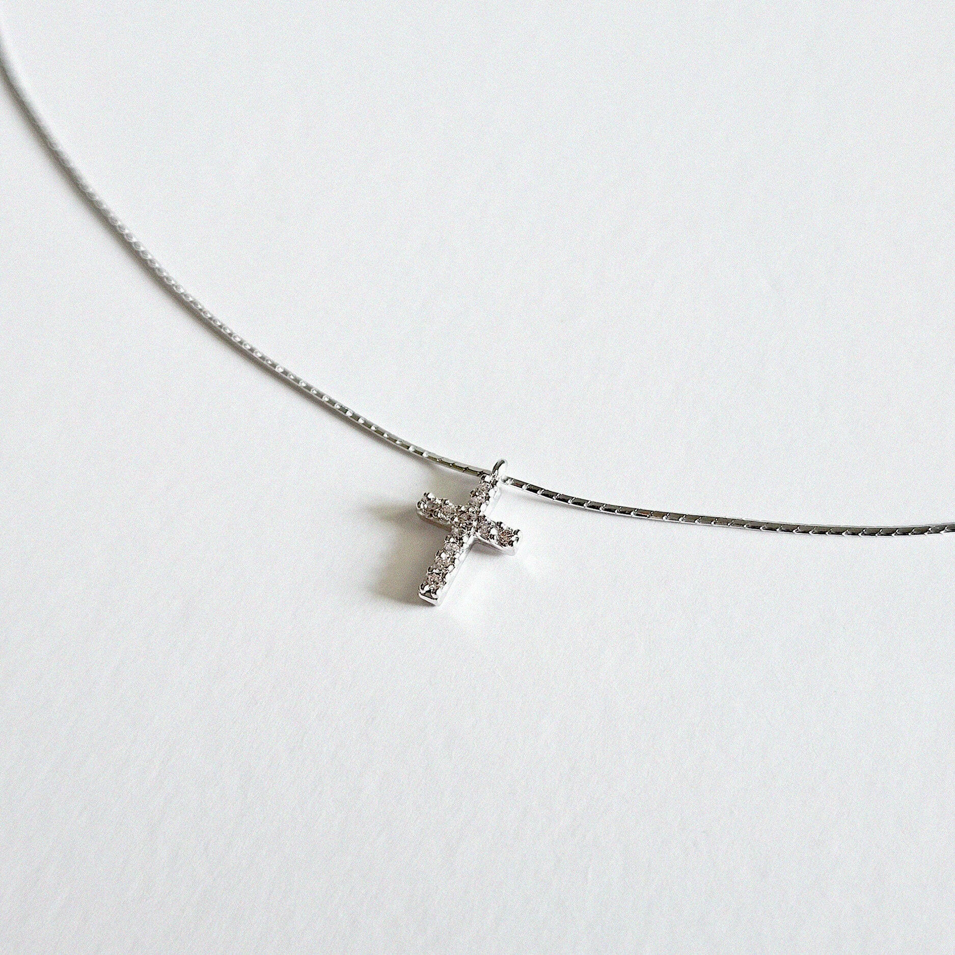 Close-up of cubic zirconia cross on fine silver snake chain with polished finish