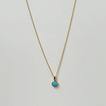 Opal pendant necklace laid flat, featuring a luminous round blue opal on a gold chain