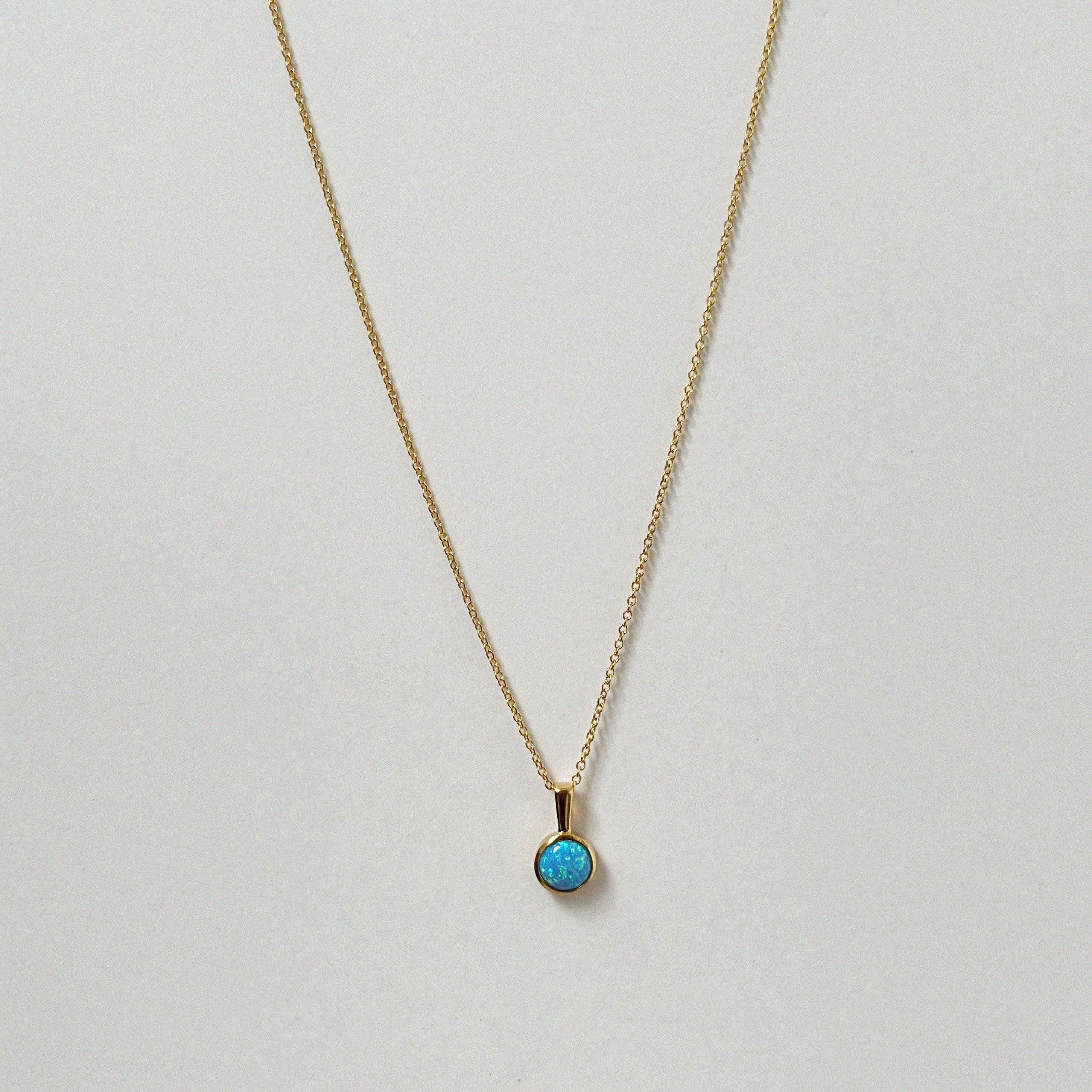 Opal pendant necklace laid flat, featuring a luminous round blue opal on a gold chain