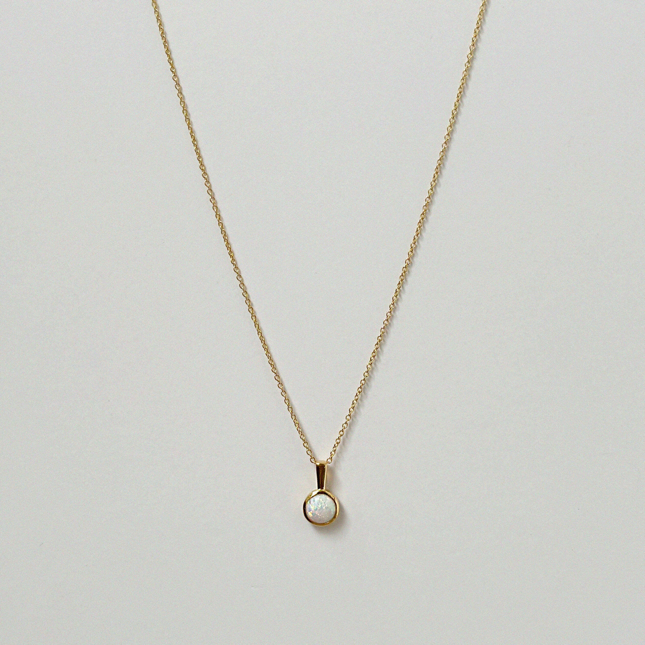 Opal pendant necklace laid flat, featuring a luminous round white opal on a gold chain