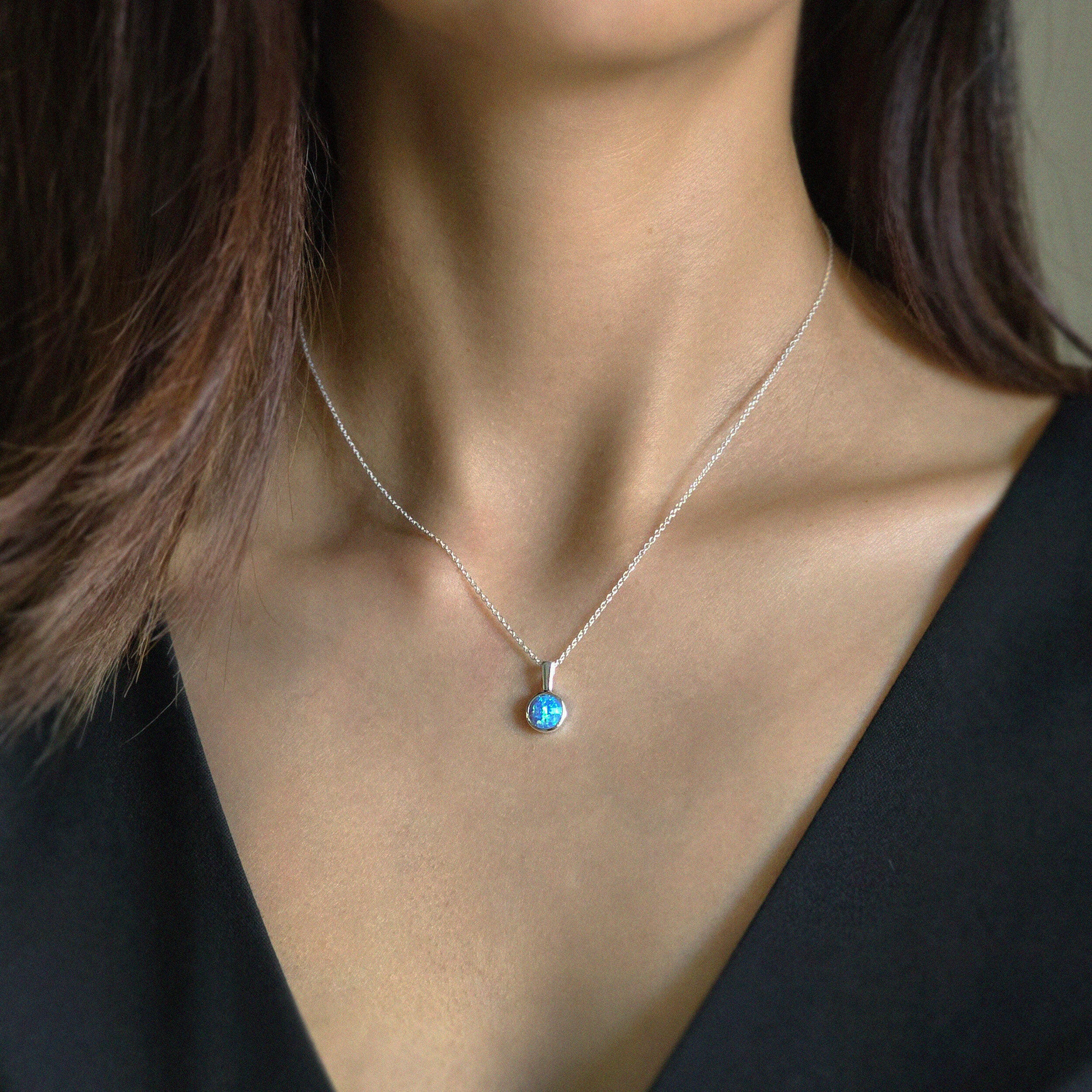 Model wearing the blue opal pendant with silver chain necklace, styled with a simple black V neck top