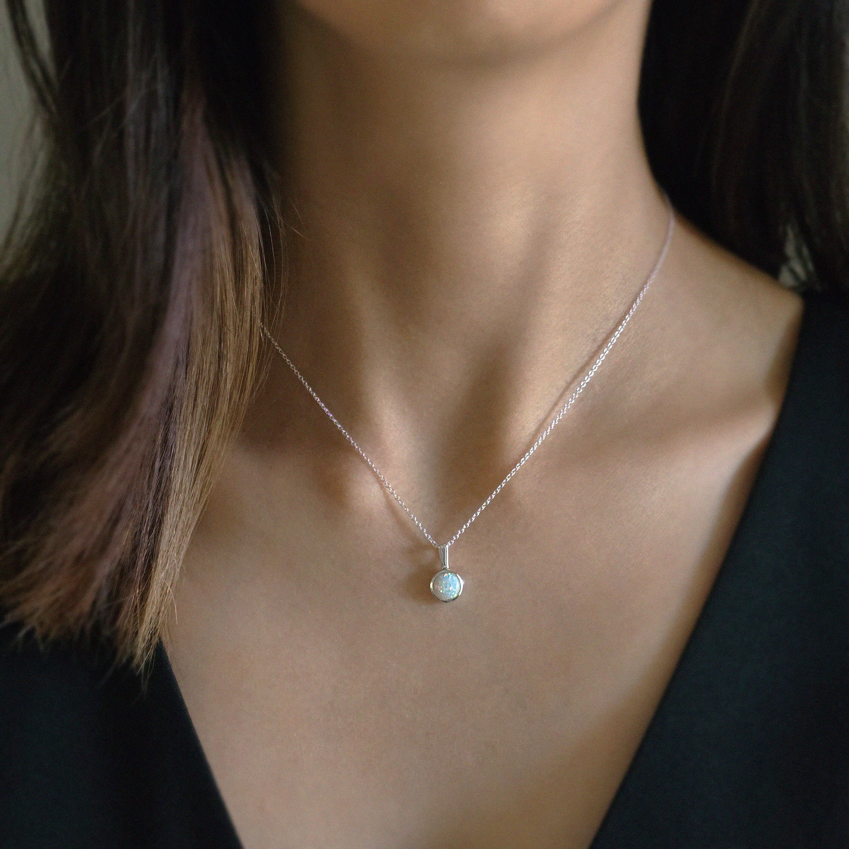 Model wearing the white opal pendant with silver chain necklace, styled with a simple black V neck top