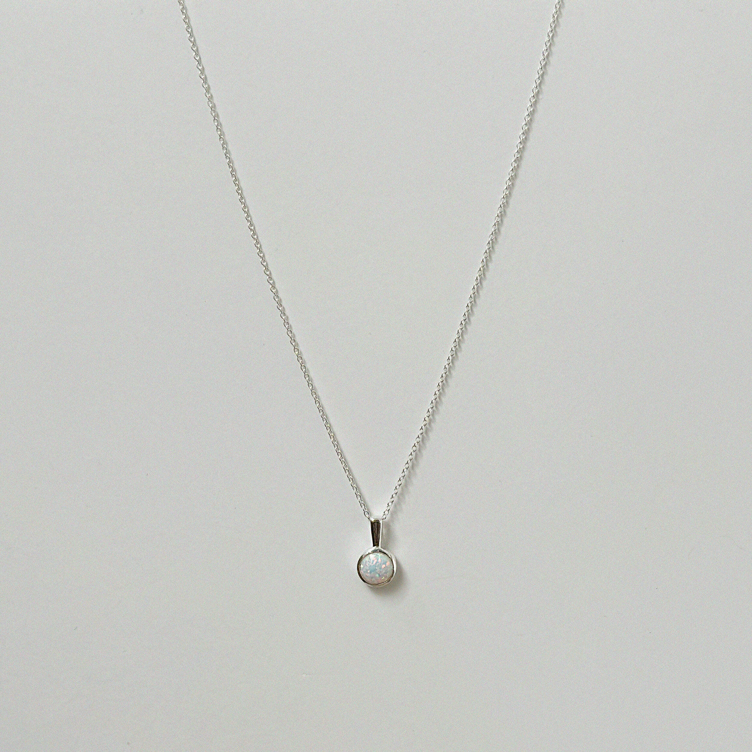 Opal pendant necklace laid flat, featuring a luminous round white opal on a silver chain