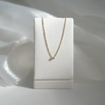 Gold necklace on a white jewelry display box against a soft white background