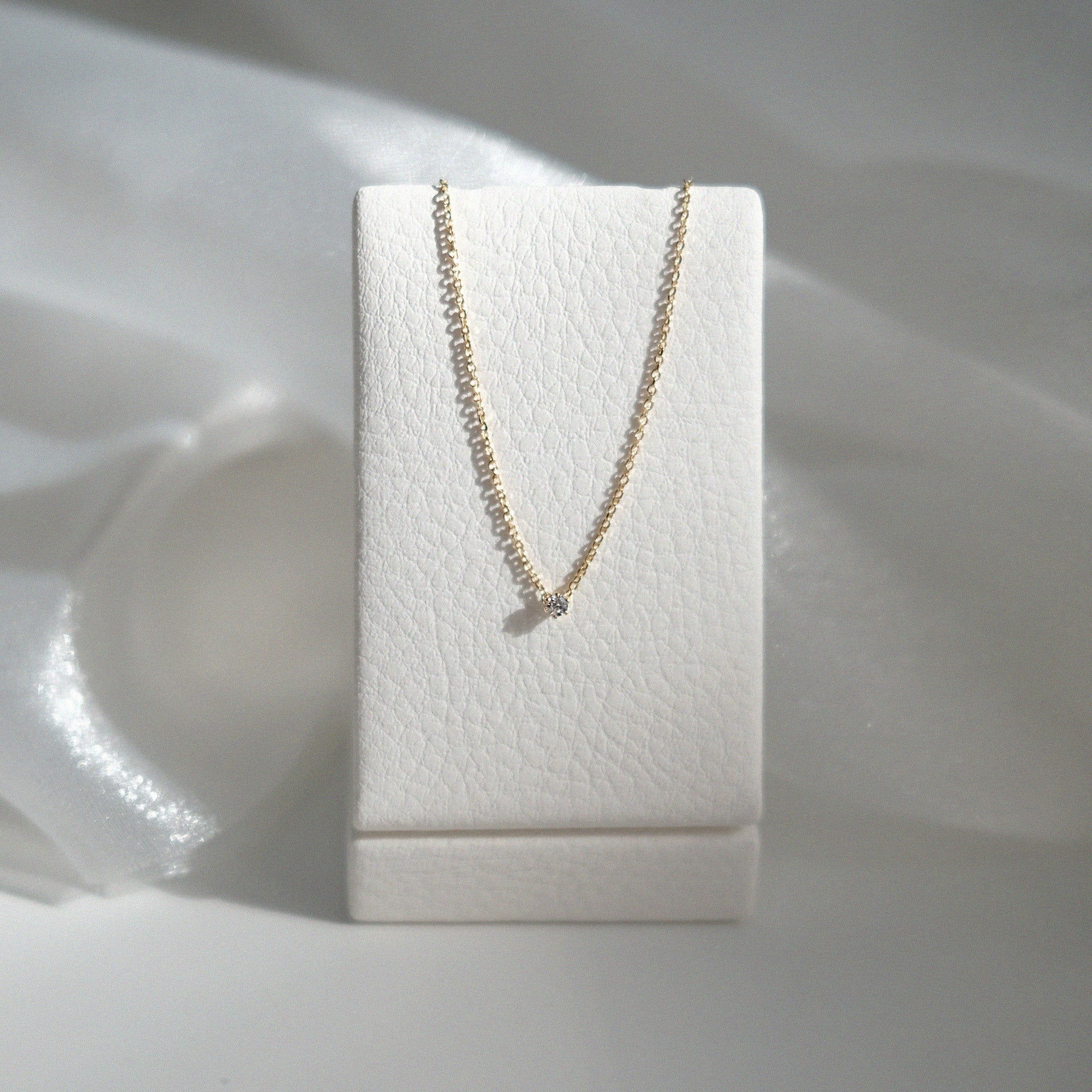Gold necklace on a white jewelry display box against a soft white background