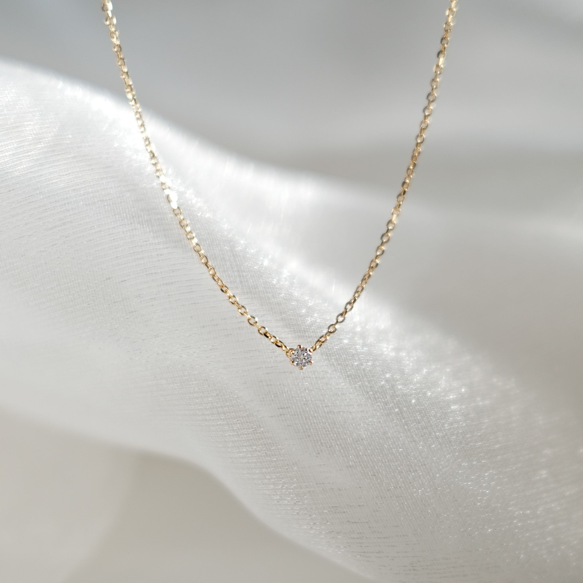 Gold necklace with a small diamond pendant on a soft white background