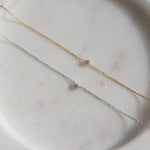 Two delicate necklaces, one gold and one silver, on a light stone surface.