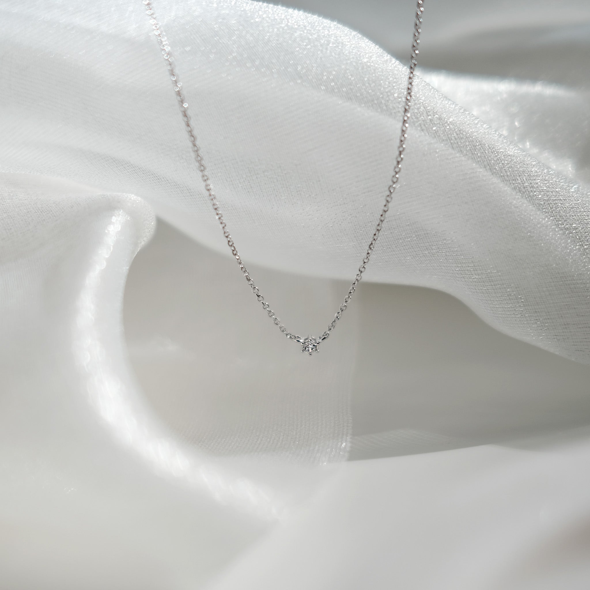 Silver necklace with a small diamond pendant on a white fabric background