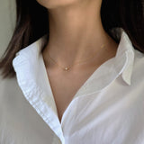Person wearing a delicate gold necklace with a white shirt