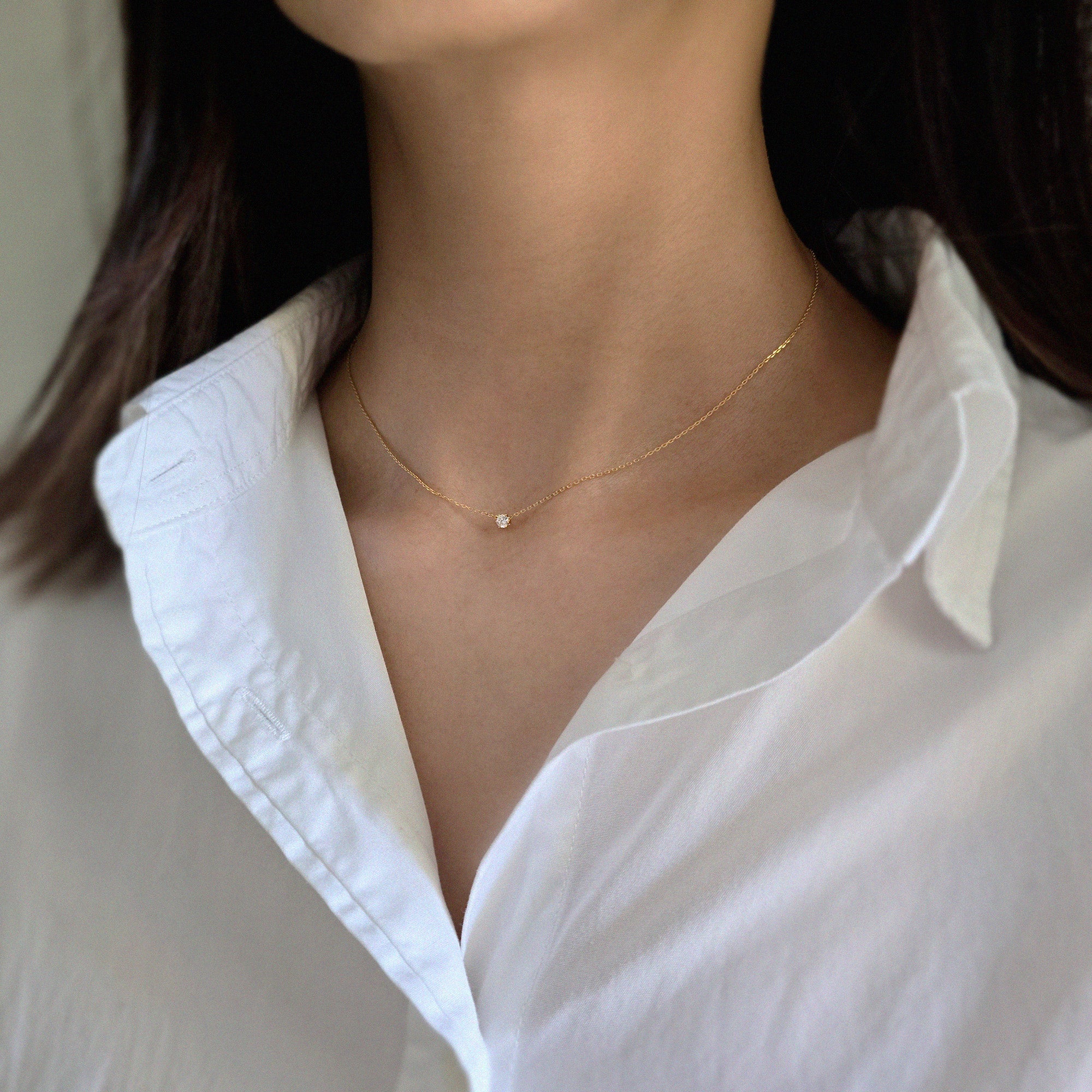 Person wearing a delicate gold necklace with a white shirt