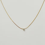 Minimalist gold snake chain with a single small crystal displayed on a neutral background