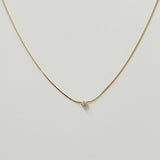 Minimalist gold snake chain with a single small crystal displayed on a neutral background