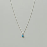 Small blue opal pendant necklace in silver laid flat on a neutral background.