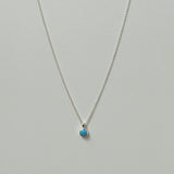 Small blue opal pendant necklace in silver laid flat on a neutral background.