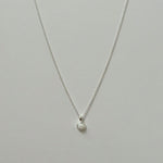 Small white opal pendant necklace in silver laid flat on a neutral background.