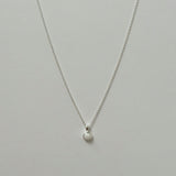 Small white opal pendant necklace in silver laid flat on a neutral background.