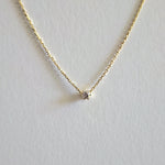 Gold necklace with a small diamond pendant on a light gray background