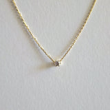 Gold necklace with a small diamond pendant on a light gray background