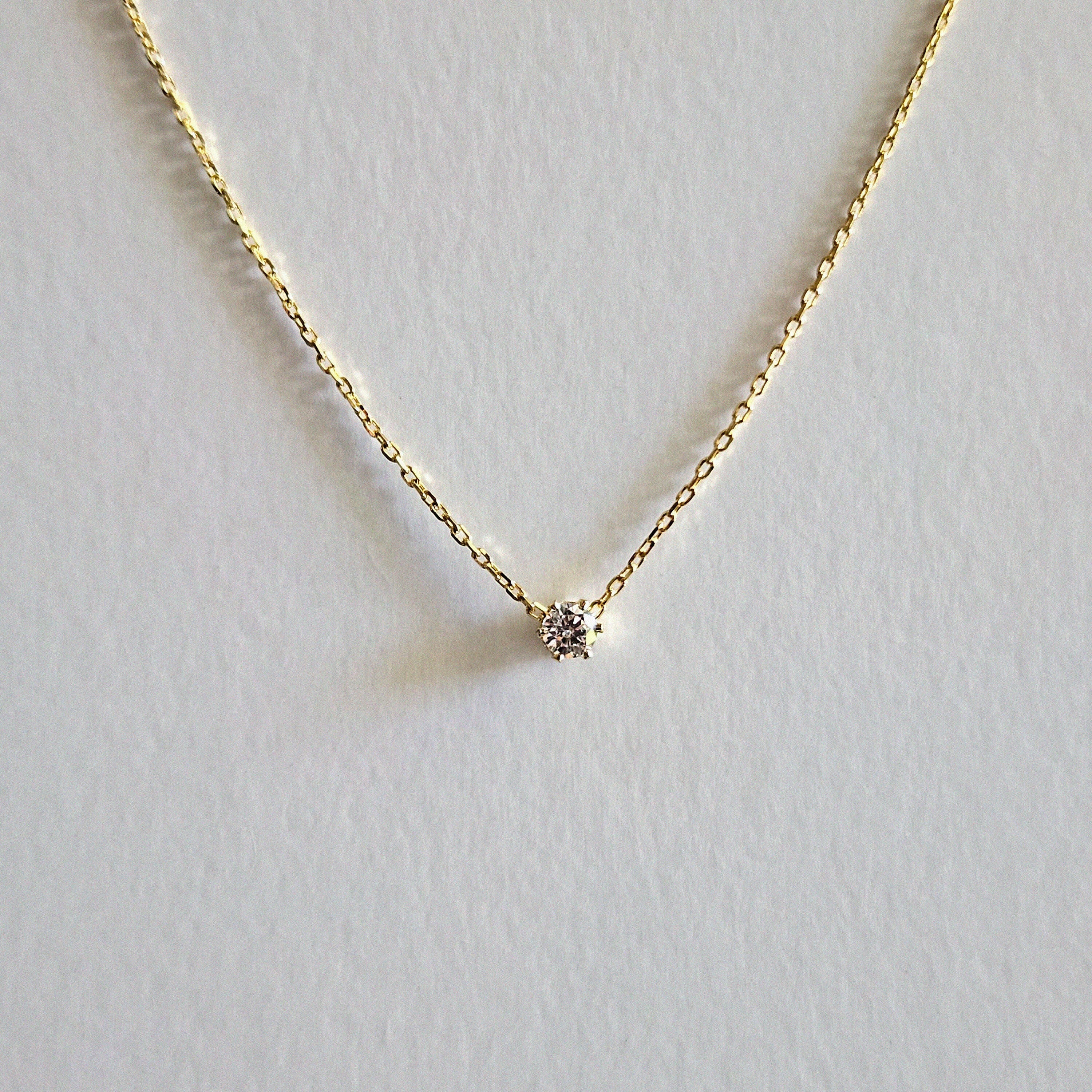 Gold necklace with a small diamond pendant on a light gray background