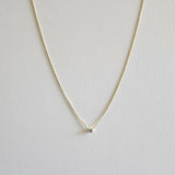 Gold necklace with a small cubic zirconia pendant on a light gray background