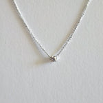 Delicate silver necklace with a small round pendant on a light gray background