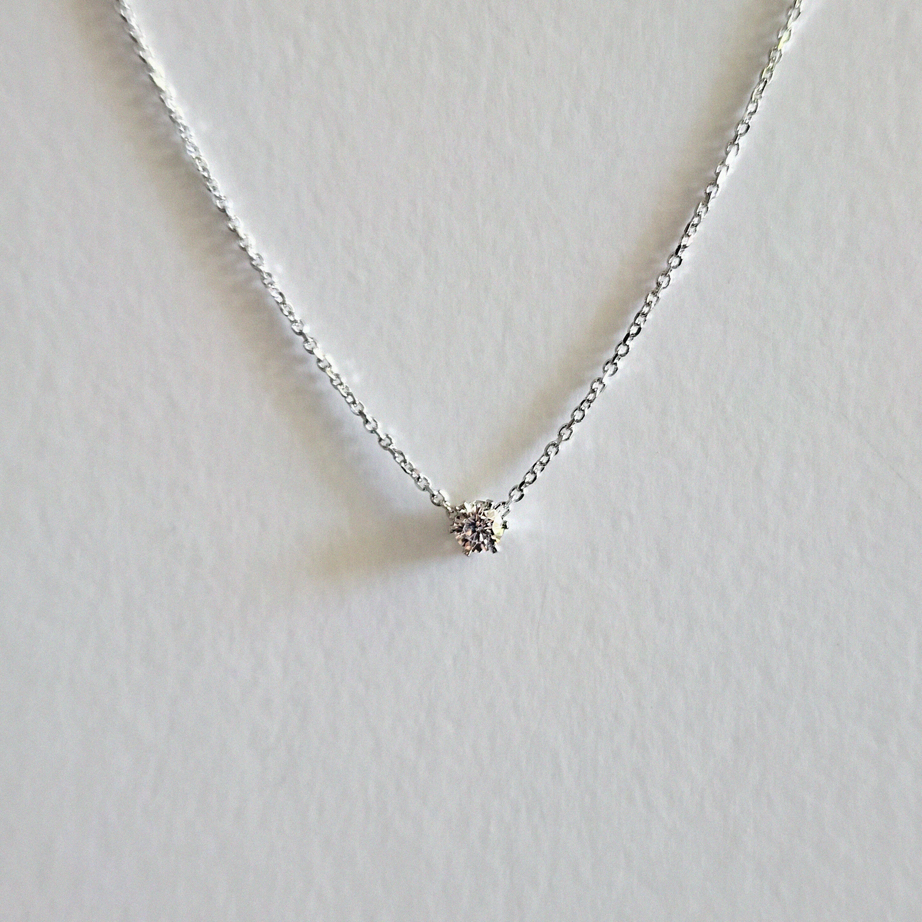 Delicate silver necklace with a small round pendant on a light gray background