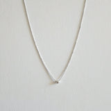 Silver necklace with a small round cubic zirconia pendant on a light gray background