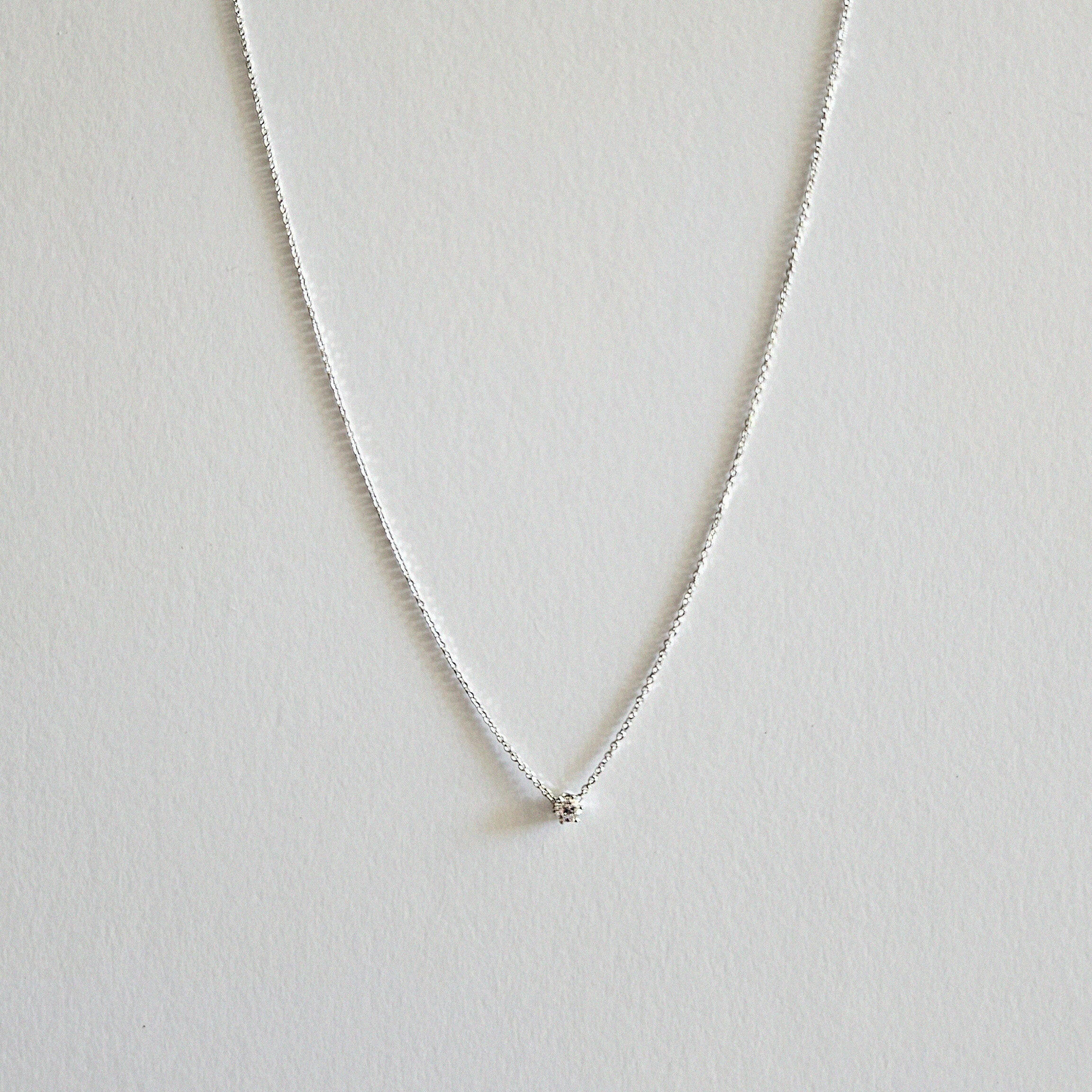 Silver necklace with a small round cubic zirconia pendant on a light gray background