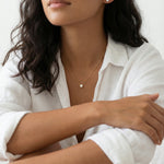 Woman wearing a delicate gold necklace with a small pendant on a plain background