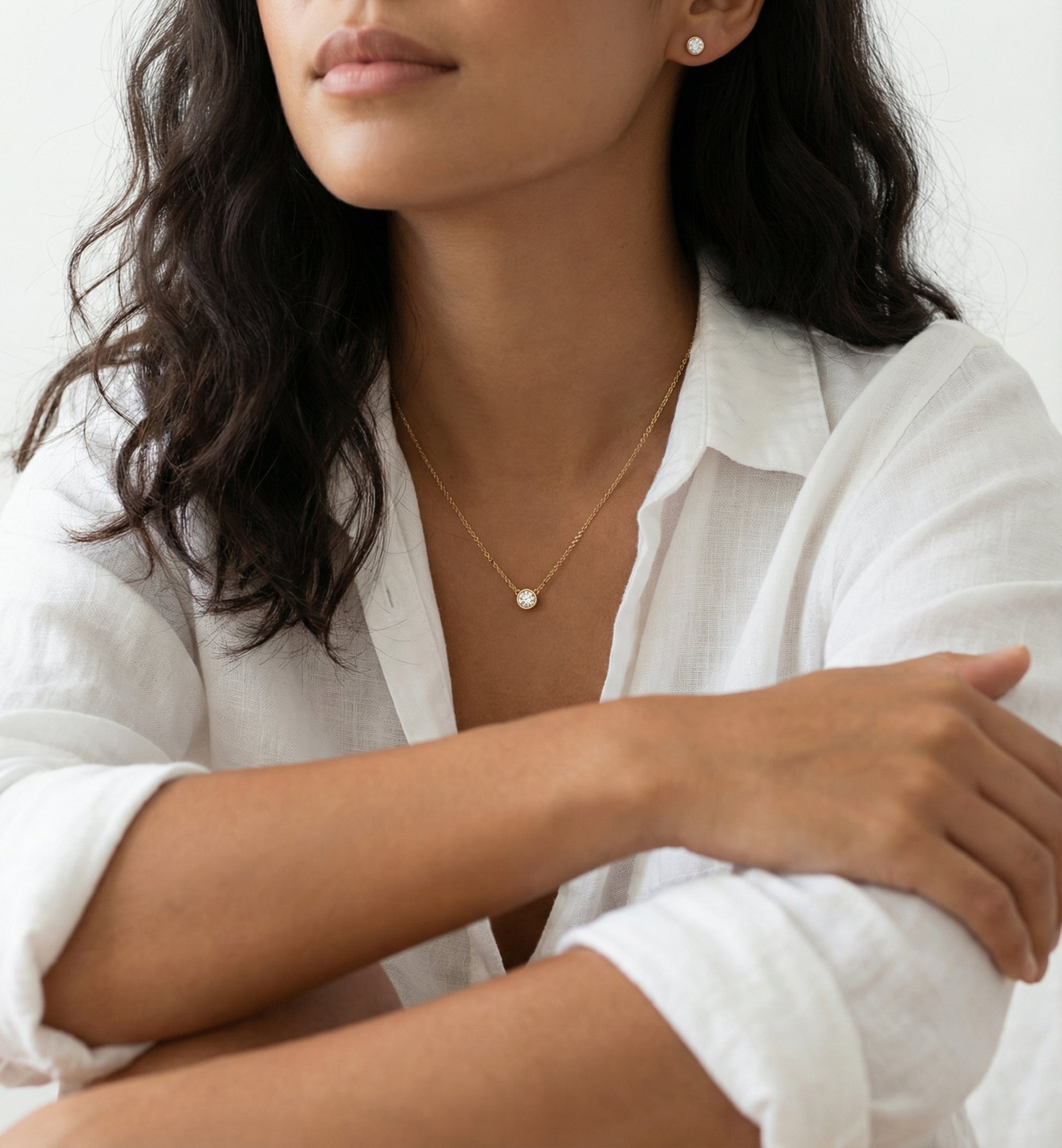 Woman wearing a delicate gold necklace with a small pendant on a plain background