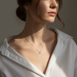 Woman wearing a white shirt and a delicate necklace with a small pendant against a neutral background