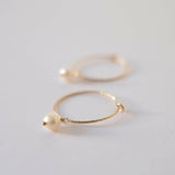 Side macro shot of freshwater pearl hanging from thin textured hoop