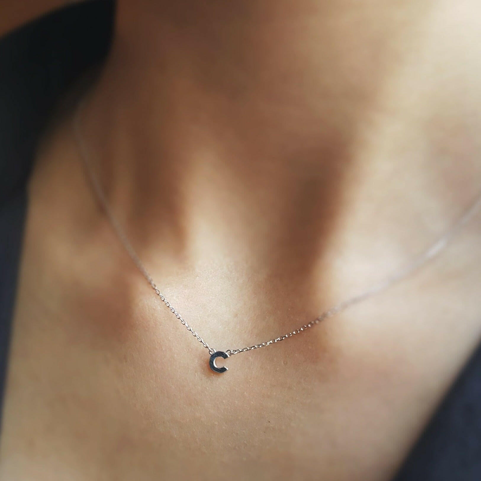 Necklace with a small letter 'T' pendant on a person's neck